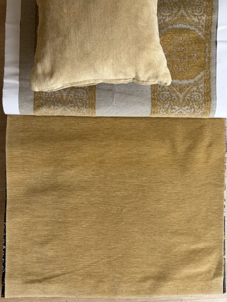 Muestra de chenilla lisa en tono oro y mostaza junto a un tejido dorado con dibujo