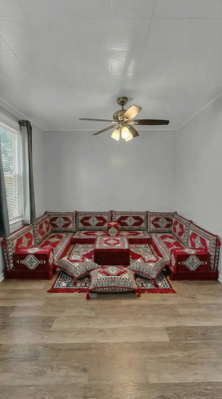 Red and cream kilim floor seating set in a U shape with ottoman and floor cushions below a ceiling fan