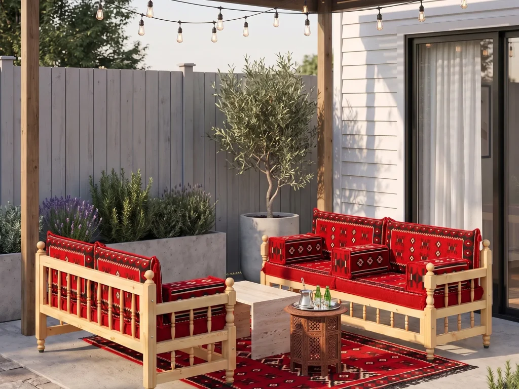 Two wooden benches with red kilim cushions on a backyard patio with an olive tree, lavender and a tea tray