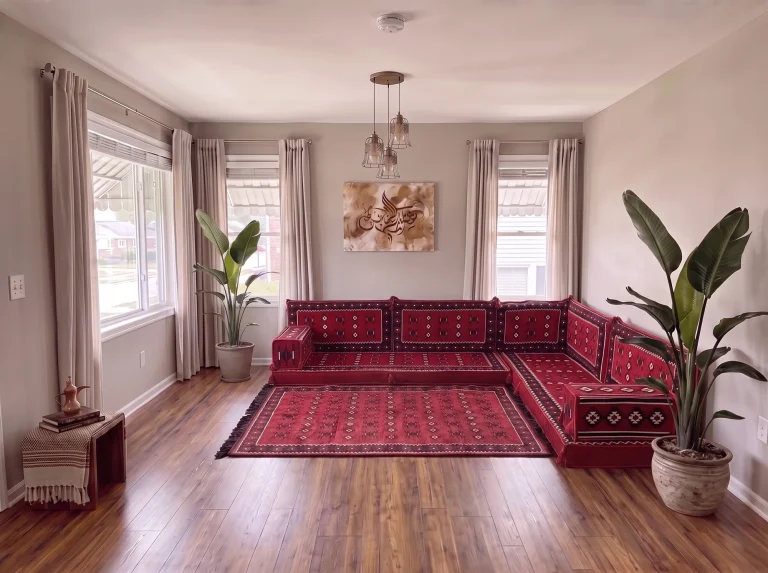 Red sadu-pattern Arabic floor couch in an L shape with a matching rug, between two potted plants