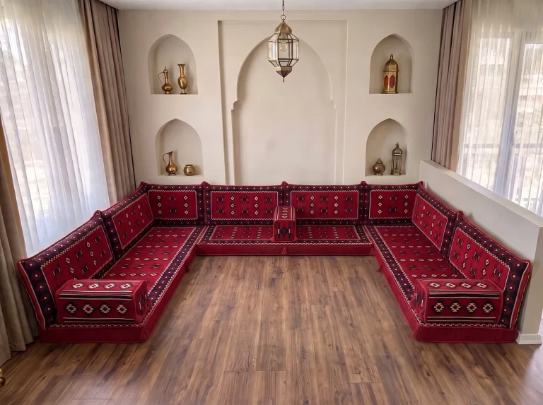 Red floor seating set with sadu-pattern cushions in a U shape on a bare wooden floor in an arched-niche room