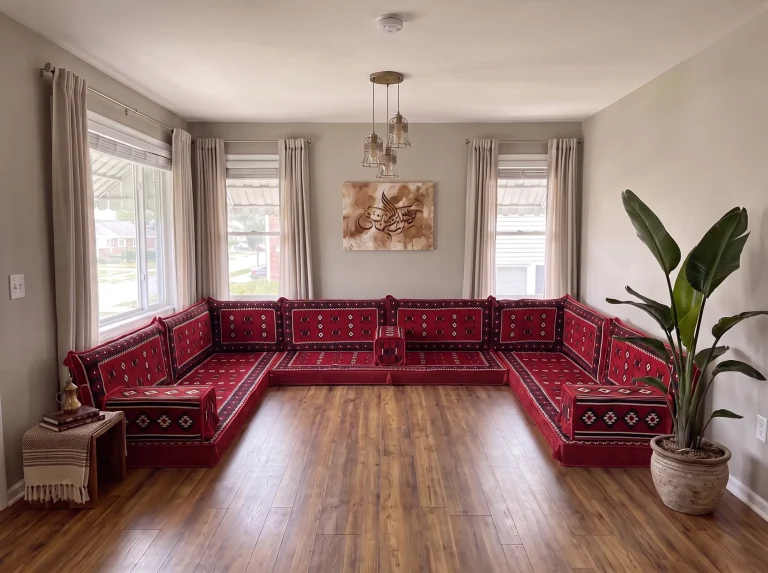 Red sadu-weave Arabic sofa running along three walls of a grey living room in a U shape, floor bare