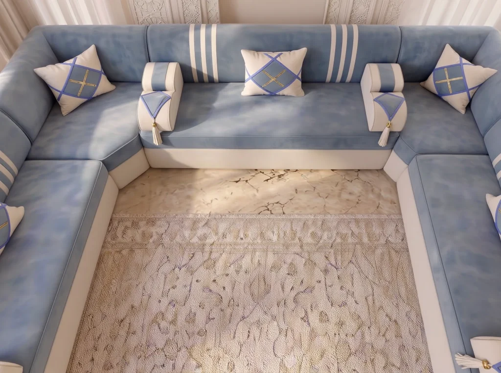 Tight overhead view of a U-shaped sky blue majlis sofa with cream armrests and diamond cushions around a rug