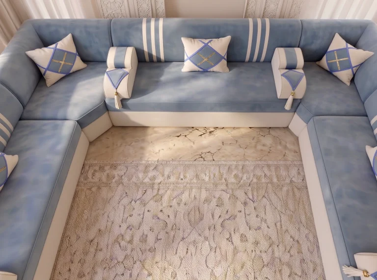 Tight overhead view of a U-shaped sky blue majlis sofa with cream armrests and diamond cushions around a rug