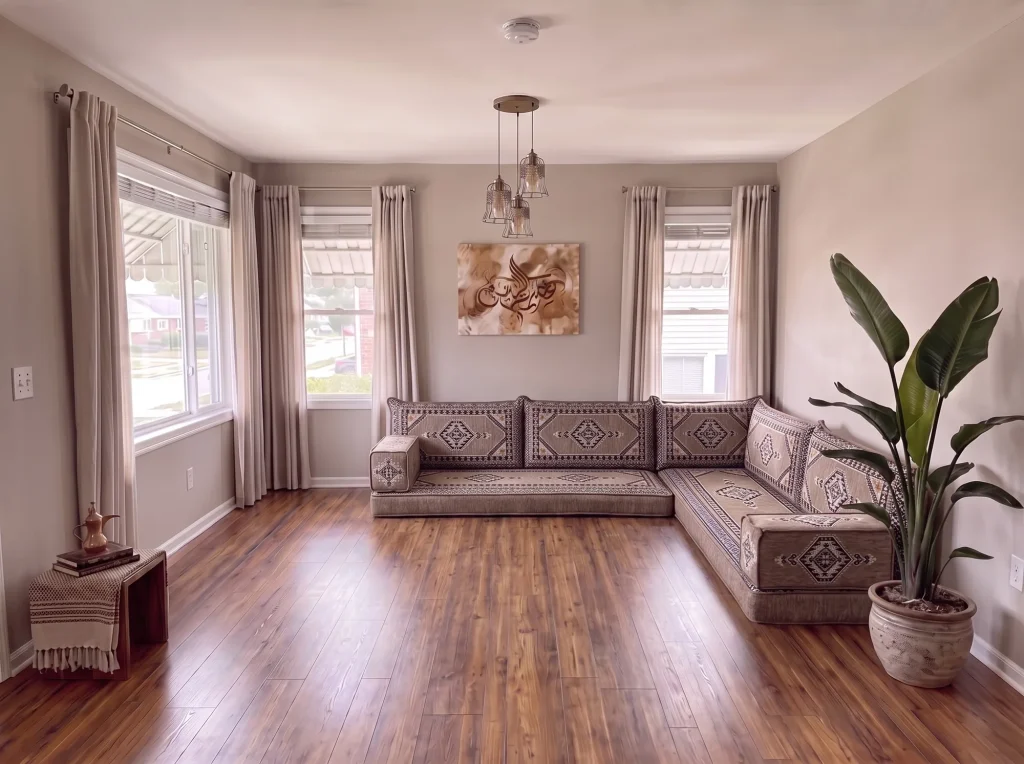Taupe and black kilim L-shaped floor seating set on a bare wood floor in a sunlit living room with a tall potted plant