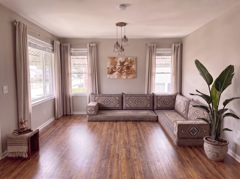 Taupe and black kilim L-shaped floor seating set on a bare wood floor in a sunlit living room with a tall potted plant