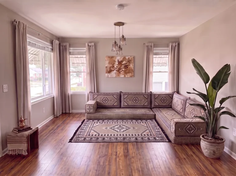 Taupe and black kilim L-shaped floor sofa set with a matching fringed rug in a sunlit living room with a tall potted plant