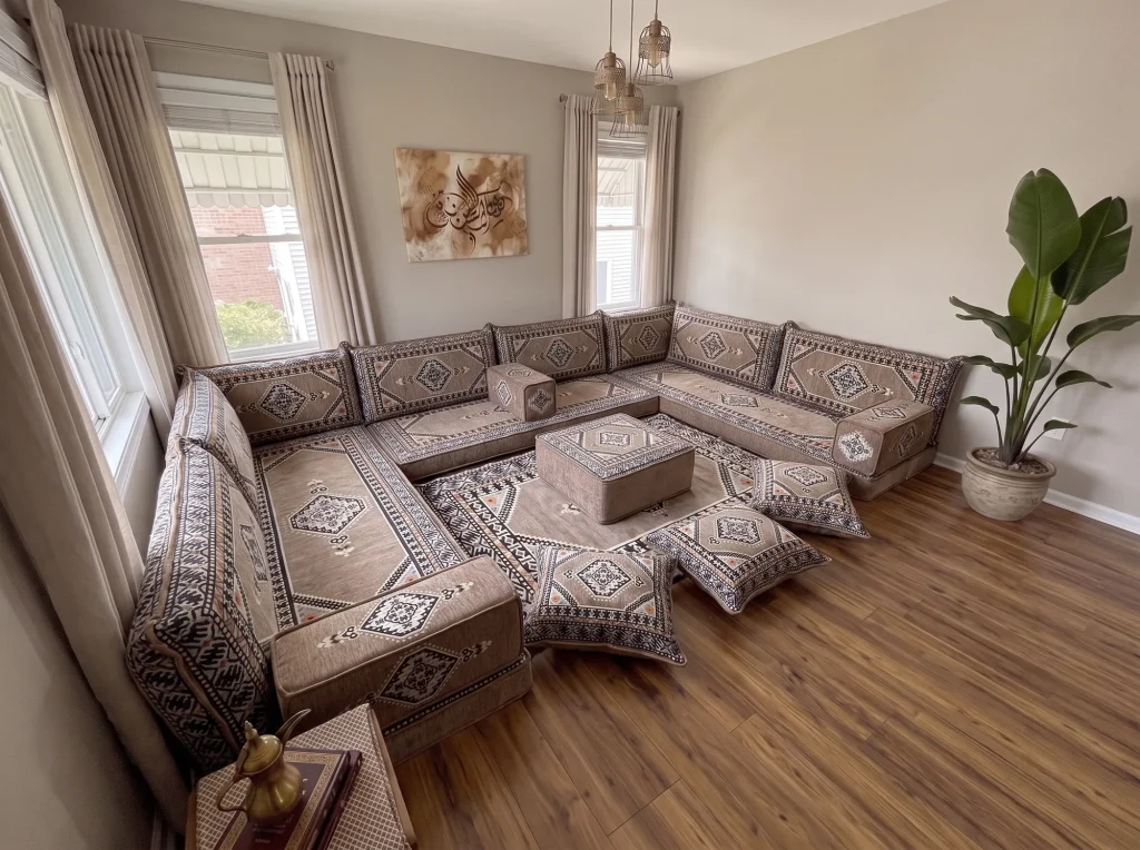 Taupe and black kilim U-shaped Arabic floor sofa with rug, ottoman and floor cushions in a sunlit living room, high corner view