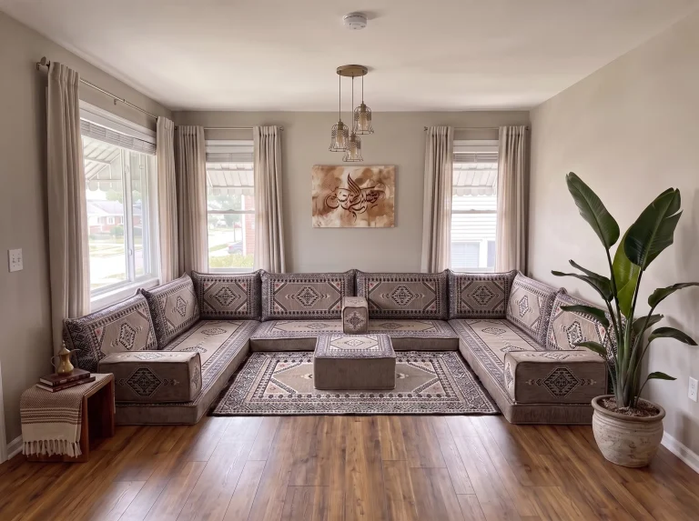 Taupe and black kilim U-shaped Arabic sofa with matching rug and ottoman in a sunlit living room with a tall potted plant