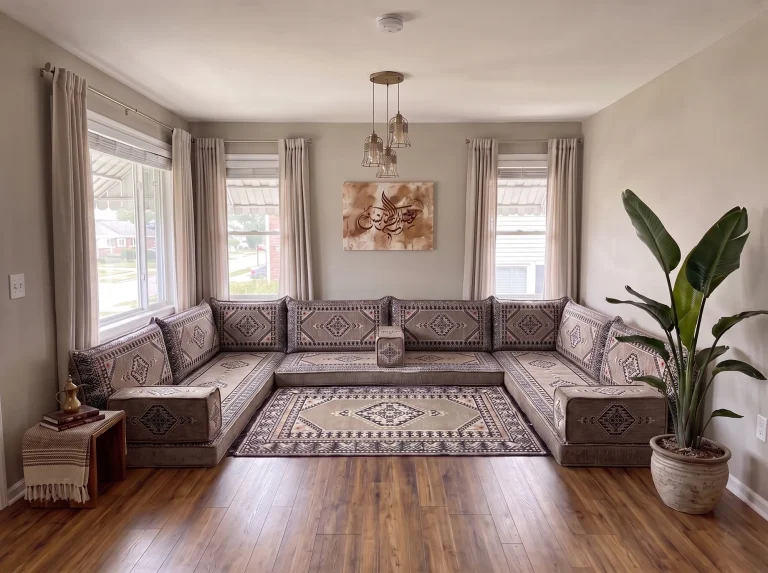 Taupe and black kilim U-shaped Arabic floor sofa with a matching fringed rug in a sunlit living room with a tall potted plant