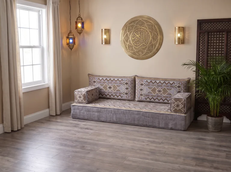 Thick gray and gold kilim-pattern Arabic sofa as a single row on a bare wood floor under a brass calligraphy wall plate