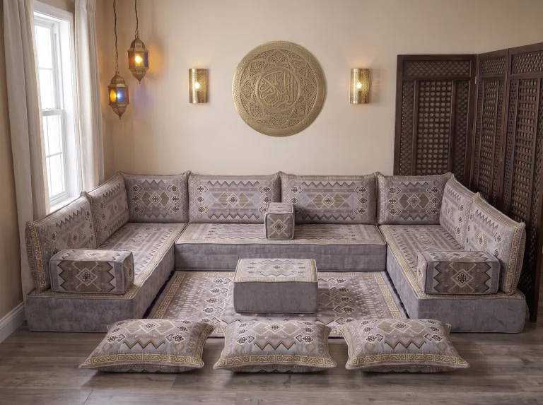 Thick gray and gold kilim Arabic floor sofa in a U shape with rug, ottoman and floor cushions below a brass wall plate