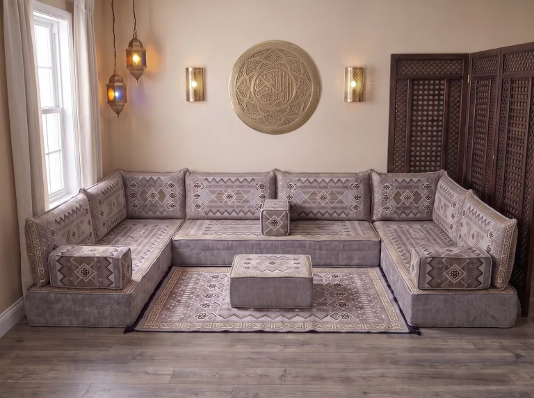 Thick gray and gold kilim-pattern floor sofa set in a U shape with matching rug and ottoman below a brass wall plate