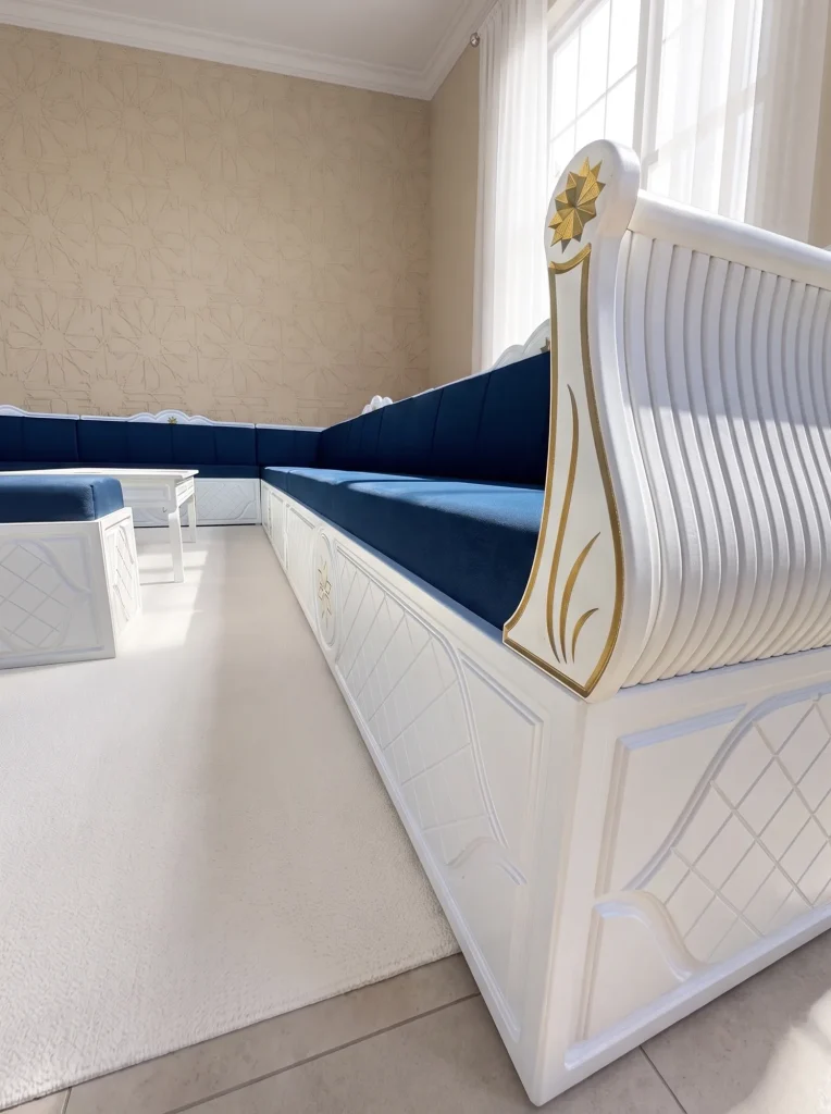 The end panel of a white carved frame with a gilded star and fluted scroll, beside a navy velvet seat
