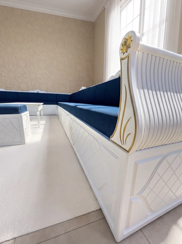 White carved wooden majlis end panel with a gold star and fluted scroll beside navy velvet seating